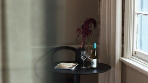 A corner of a room with a table set for two, a chair, a small stool, and a window with curtains. - Empire Hotel  (Annandale)