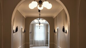A hallway with a chandelier, white walls, and a window with sheer curtains. - Empire Hotel  (Annandale)