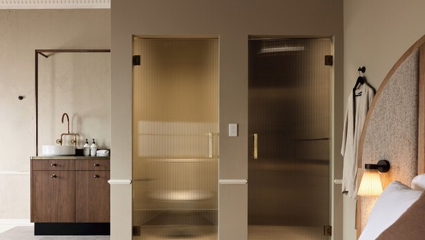 A hotel room with a bed, a wooden cabinet with toiletries, a sliding door, and a wall-mounted lamp. - Empire Hotel  (Annandale)