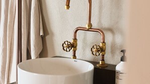 A bathroom with a round white sink, copper faucet, and a wooden cabinet below. - Empire Hotel  (Annandale)