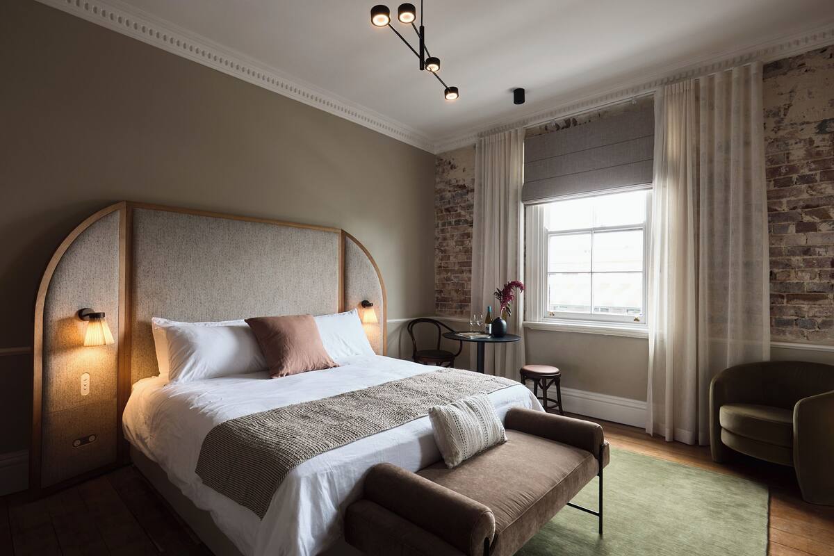 A bedroom with a large bed, a small table with a vase, and a chair.