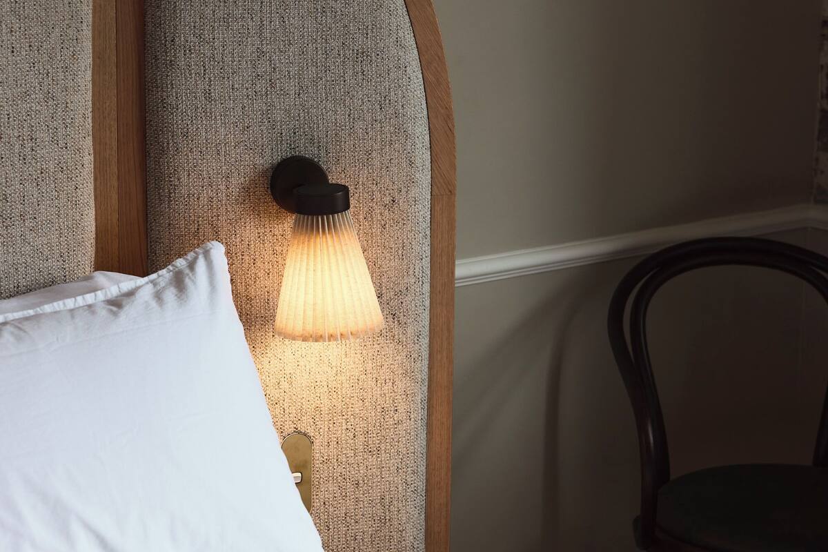A neatly made bed with a white pillow and a headboard with a textured wall panel.
