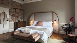 A bedroom with a large bed, a wooden bench, a small table with a vase, and a brick wall. - Empire Hotel  (Annandale)