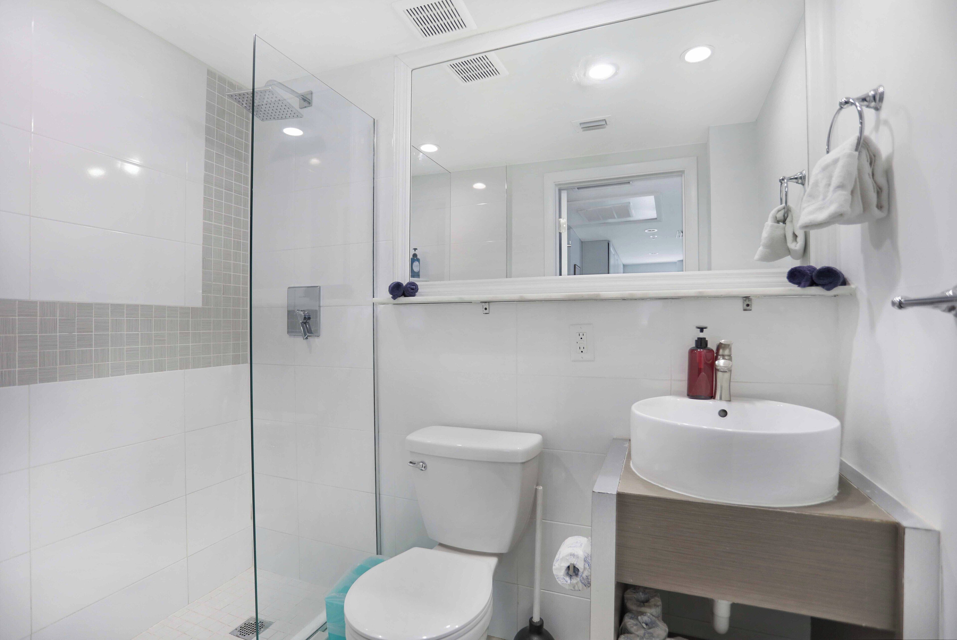 Un baño moderno con ducha de vidrio, inodoro blanco y lavamanos con espejo.