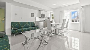 A modern living room with a glass coffee table, a green sofa, and a dining area with white chairs. - NEW LISTING! 4 Bedroom Combined Suites (Miami Beach)