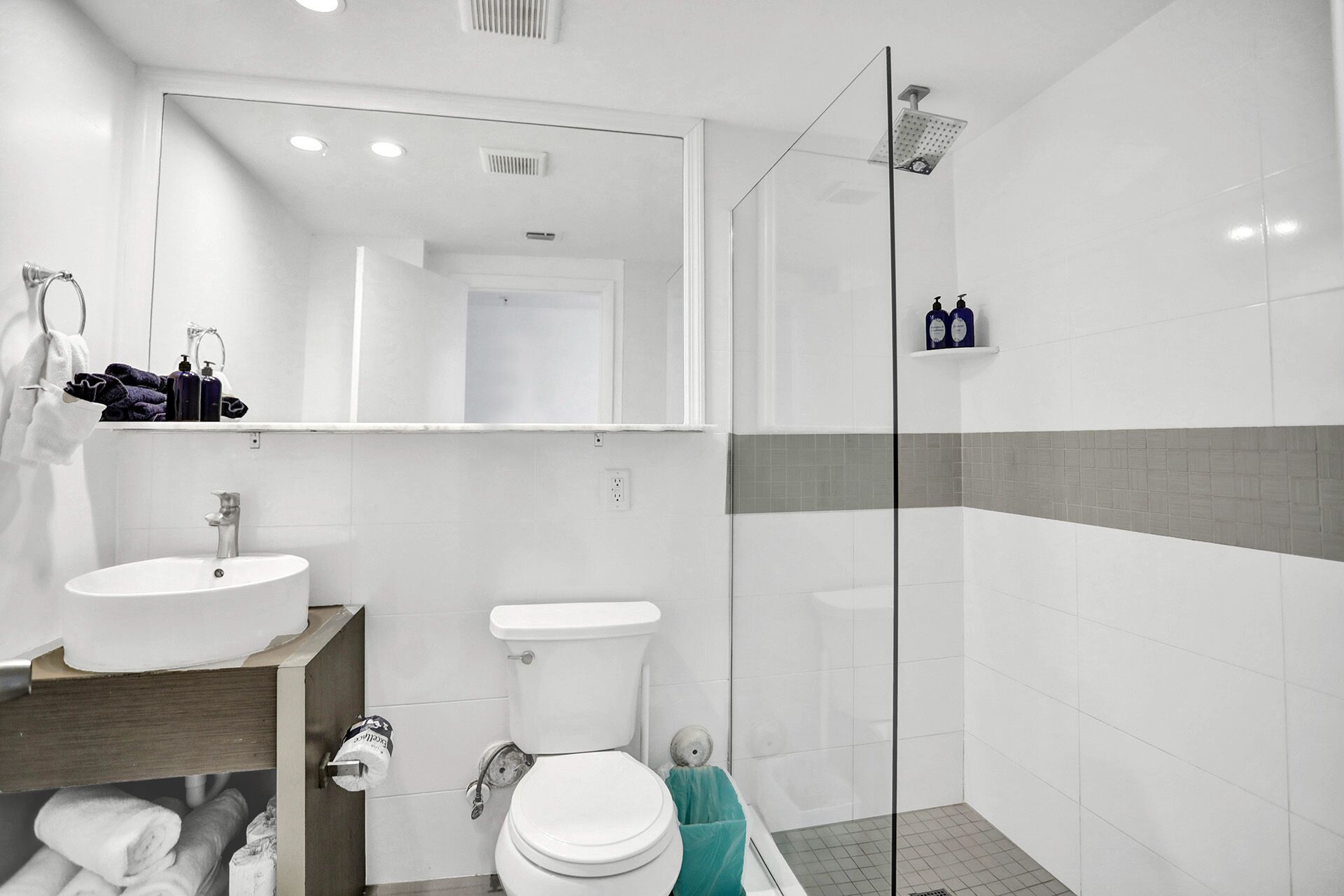 Une salle de bain moderne avec un lavabo, des toilettes et une douche, le tout de couleur blanche. Un miroir est placé au-dessus du lavabo, et un porte-serviettes contient des serviettes.
