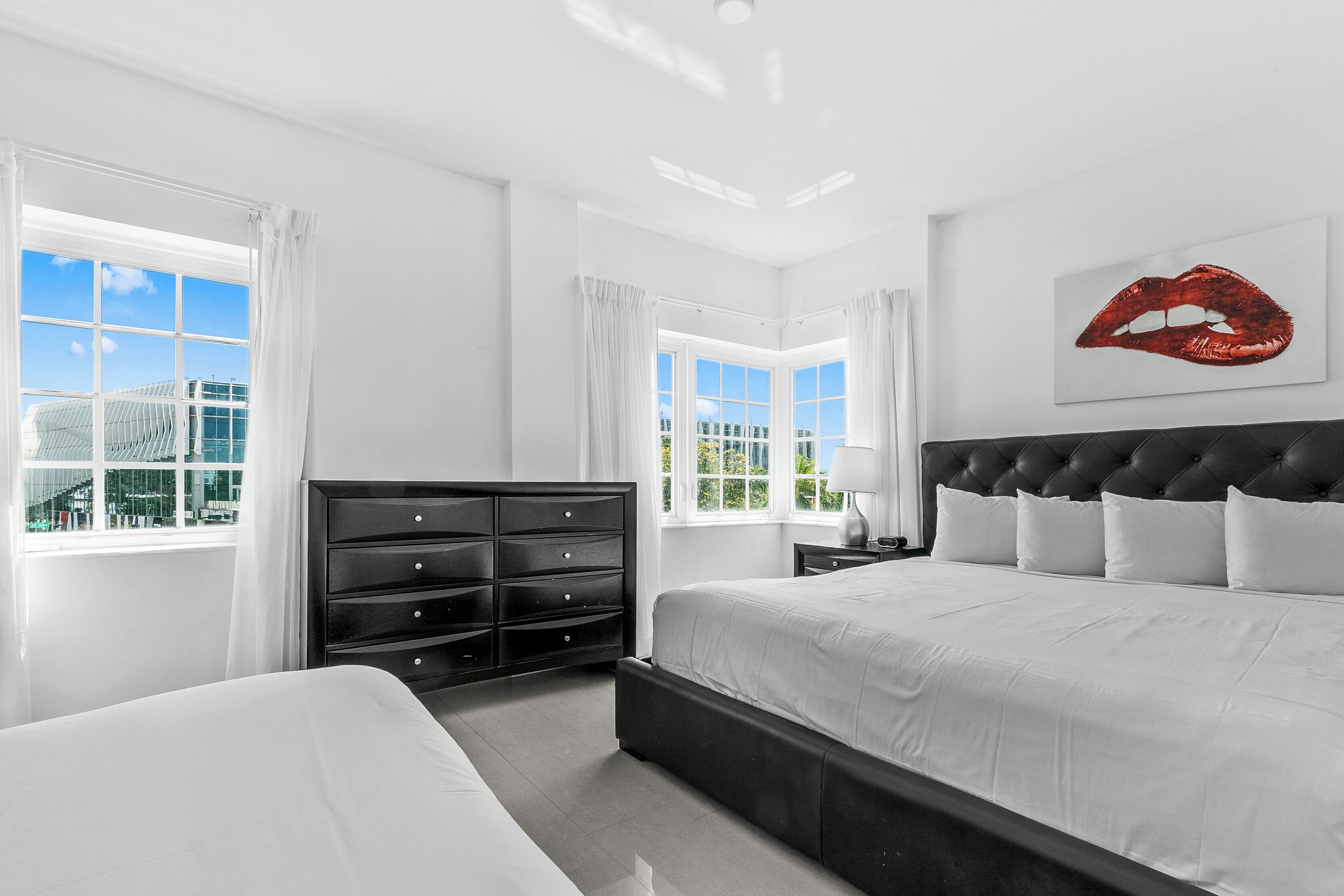 Una habitación de hotel moderna con una cama grande, un aparador negro y vistas a un edificio a través de las ventanas.