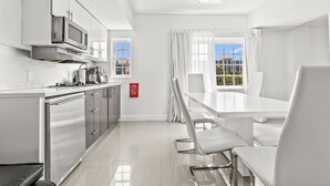 A modern kitchen with stainless steel appliances, a dining area with white chairs, and large windows with curtains. - NEW LISTING! 4 Bedroom Combined Suites (Miami Beach)
