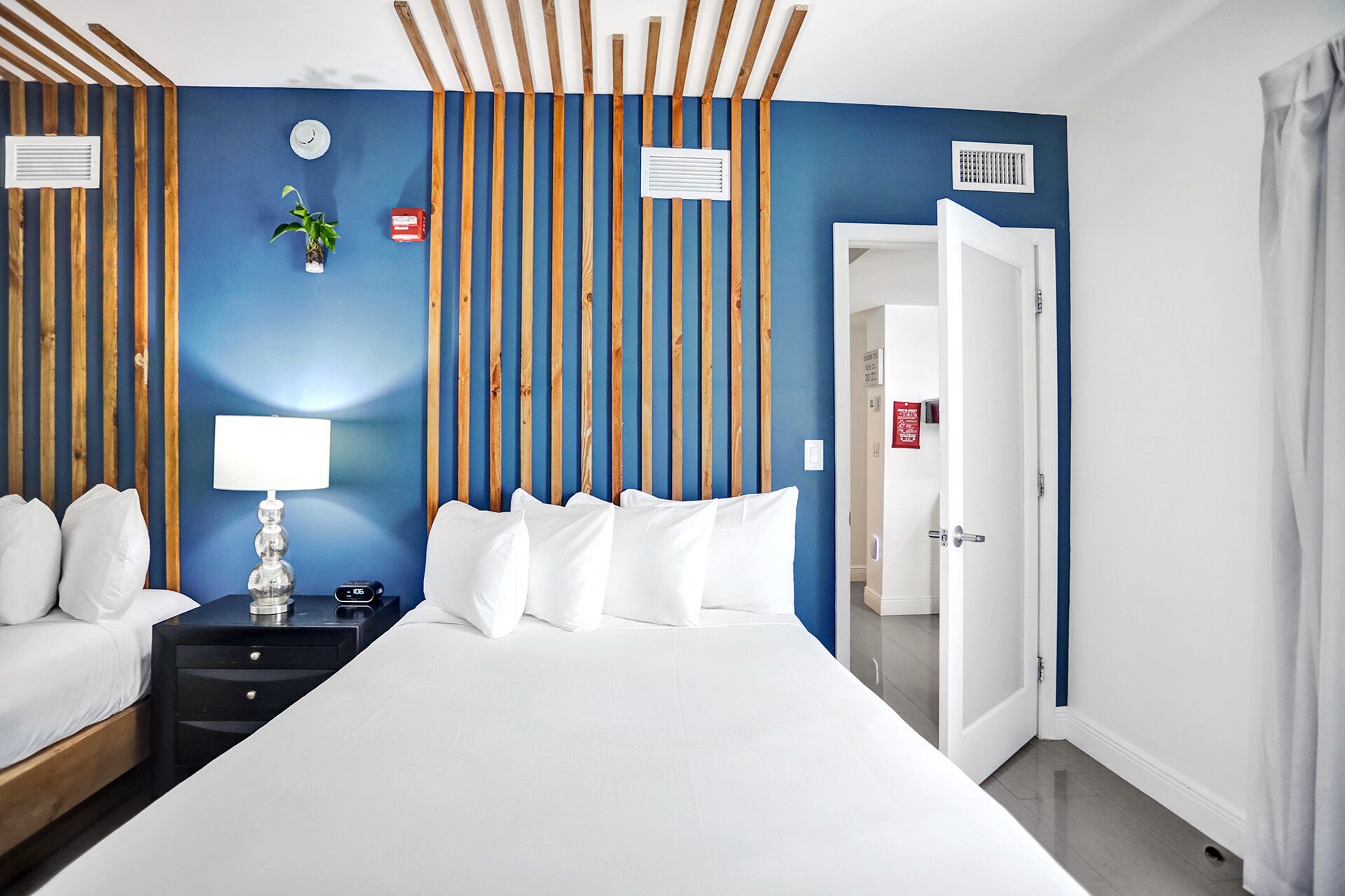 Ein Hotelzimmer mit Bett, Nachttisch, Lampe und einer Wand mit vertikalen Holzbalken.