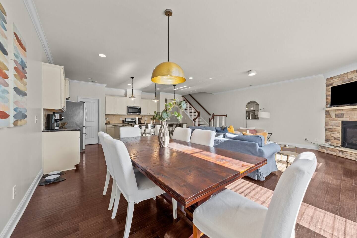 A spacious living area with a wooden dining table, white chairs, a sofa, and a fireplace.