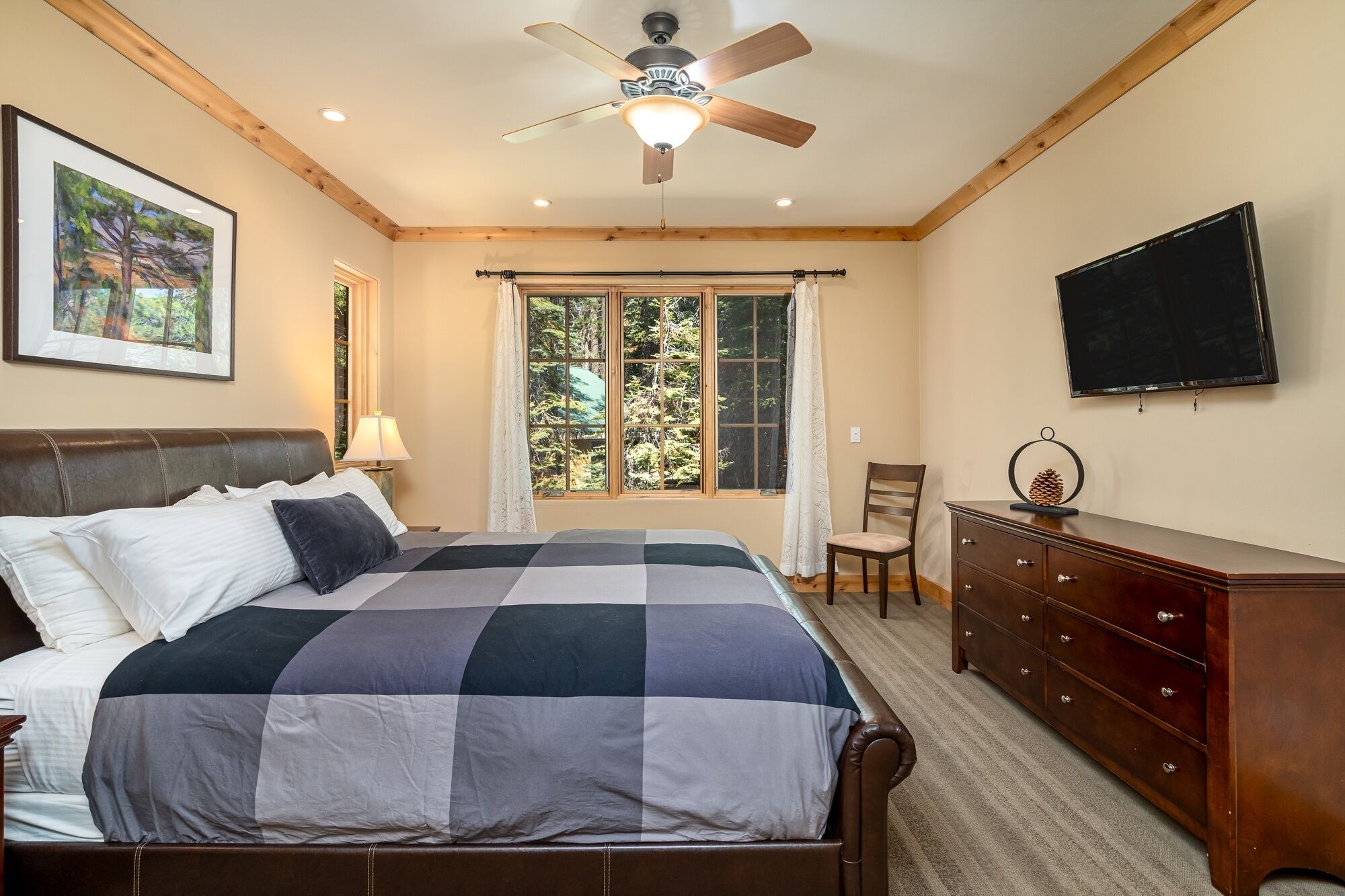 Une chambre à coucher comprenant un lit, un ventilateur de plafond, une télévision, une commode et une fenêtre avec des rideaux.