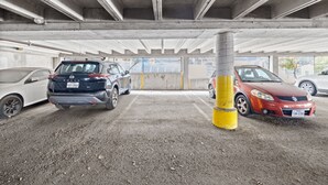 Un aparcamiento con pilares de hormigón, suelo de tierra y coches estacionados en plazas delimitadas.