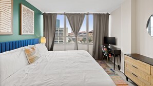 Habitación de hotel con una cama grande, un escritorio con televisor y vistas a la ciudad desde la ventana.