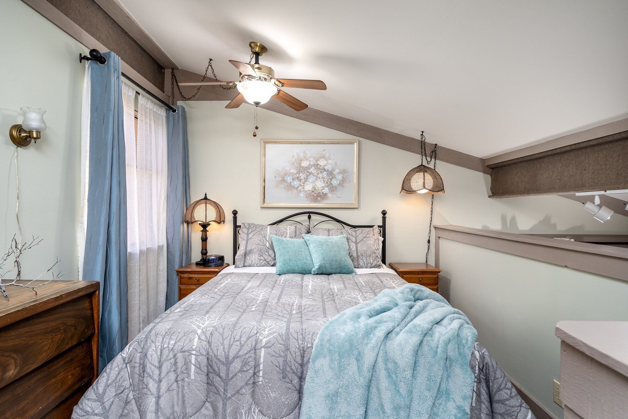 A bedroom with a bed, a ceiling fan, a bedside table with a lamp, a nightstand, and a wall-mounted shelf.