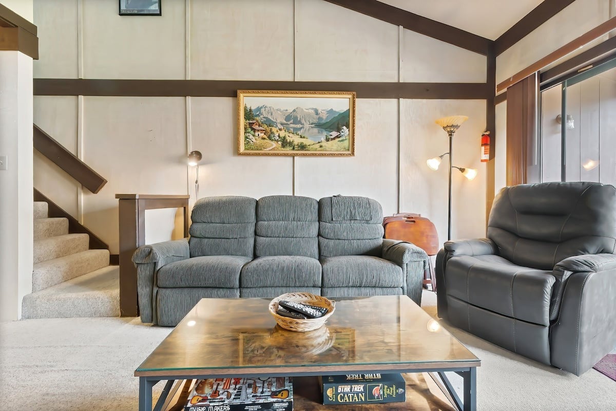 Ein Wohnzimmer mit einer Couch, einem Sessel, einem Couchtisch mit Fernbedienung und einem gerahmten Gemälde an der Wand.