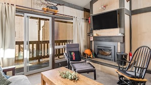 A cozy living room with a fireplace, a large window, and a sliding door leading to an outdoor area. - Bear Valley Condos by RedAwning (Arnold)
