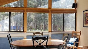 A dining area with a round table and four chairs, large windows with a view of trees, and a framed picture on the wall. - Bear Valley Condos by RedAwning (Arnold)