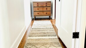 A hallway with a wooden floor, a beige and white patterned rug, a wooden dresser, and a round mirror on the wall. - Charming 1-bedroom house in lovely Mid-City Los Angeles (Los Angeles)
