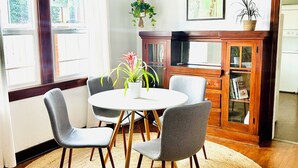 A dining area with a round table, four chairs, a ceiling fan, a wooden cabinet, and a large window with curtains. - Charming 1-bedroom house in lovely Mid-City Los Angeles (Los Angeles)