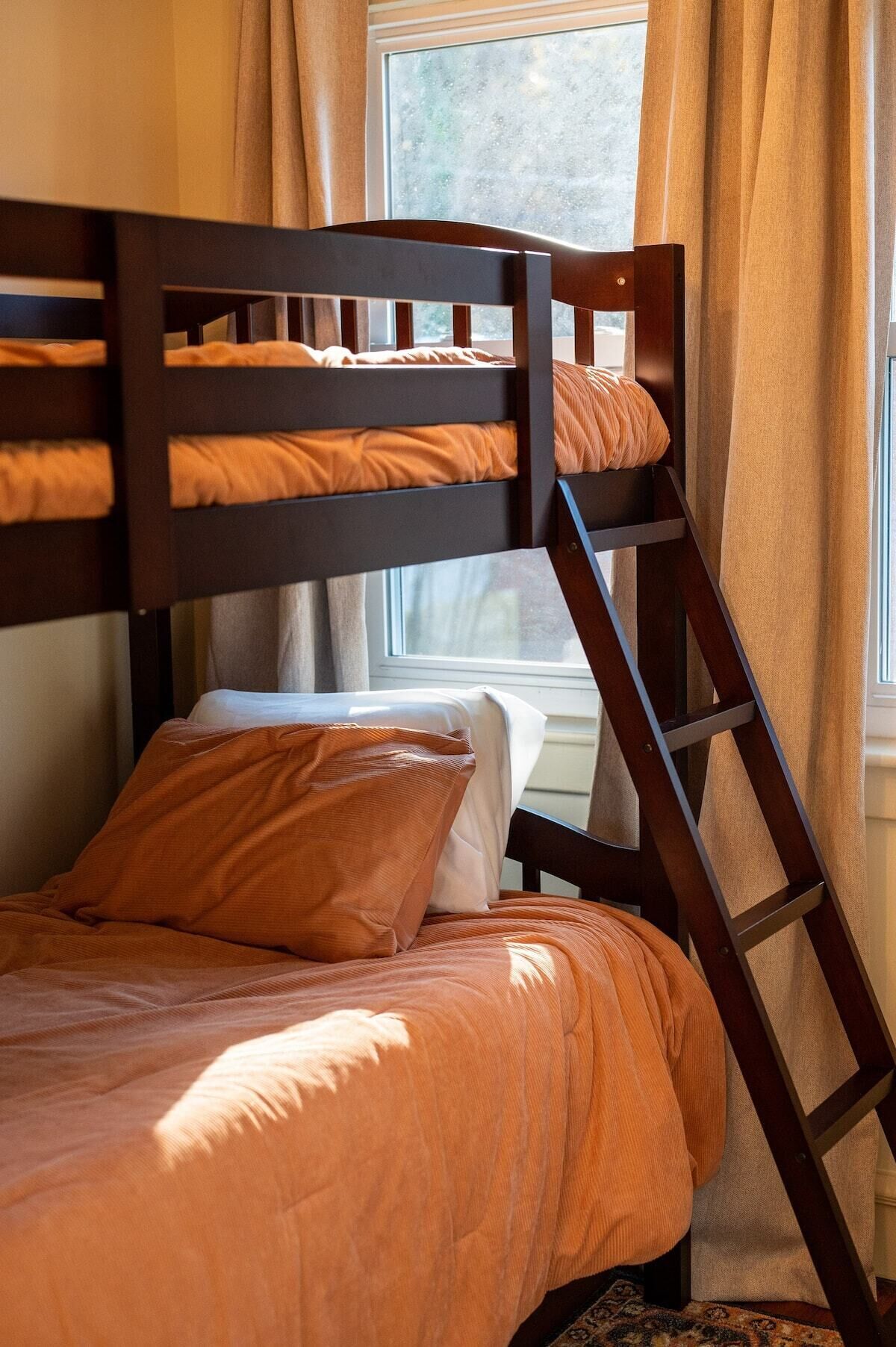 Un lit superposé à deux niveaux, une fenêtre avec des rideaux et un tapis à motifs.
