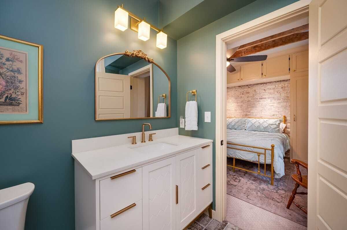 Une salle de bain avec un meuble-lavabo blanc, un grand miroir et un luminaire placé au-dessus du miroir.