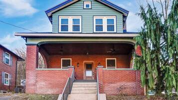 A two-story house with a front porch, brick foundation, and a small front yard.