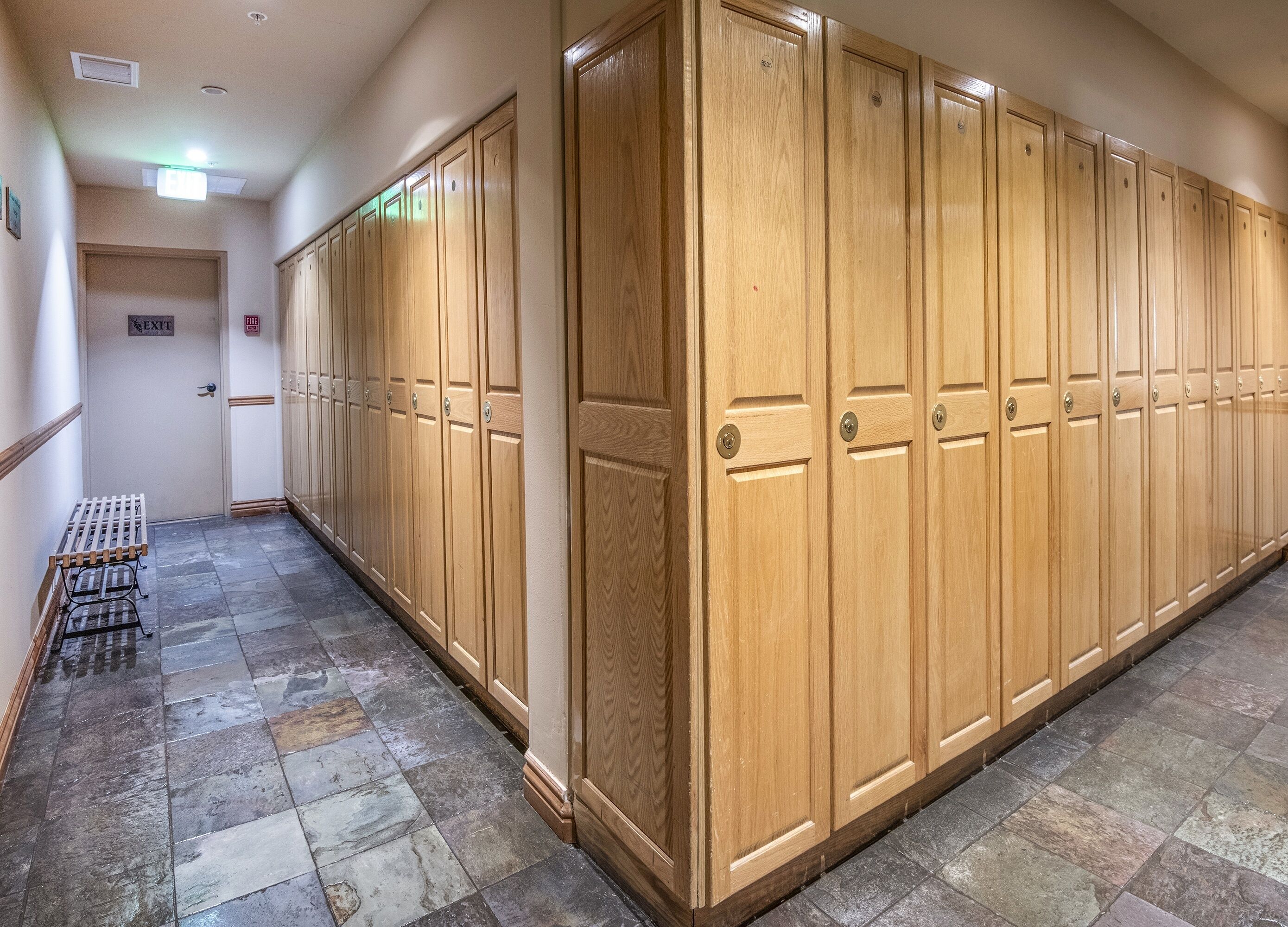 A hallway with wooden lockers, a tiled floor, and an exit sign.