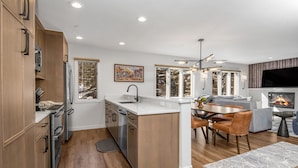 A modern kitchen with wooden cabinets, a central island, and a dining area with a fireplace. - Beaver Creek Resort CO - Townsend Place Vacation Rentals (Avon)