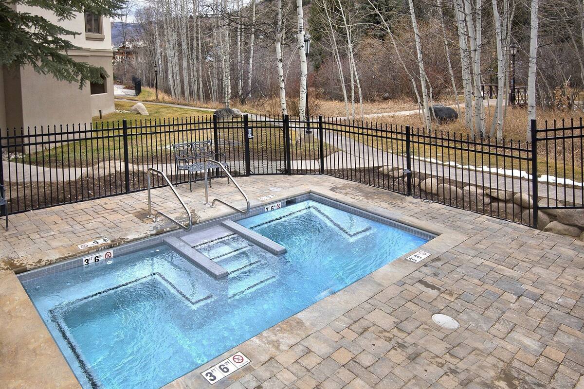 A rectangular swimming pool with a black metal fence, a ladder, and a tiled deck.