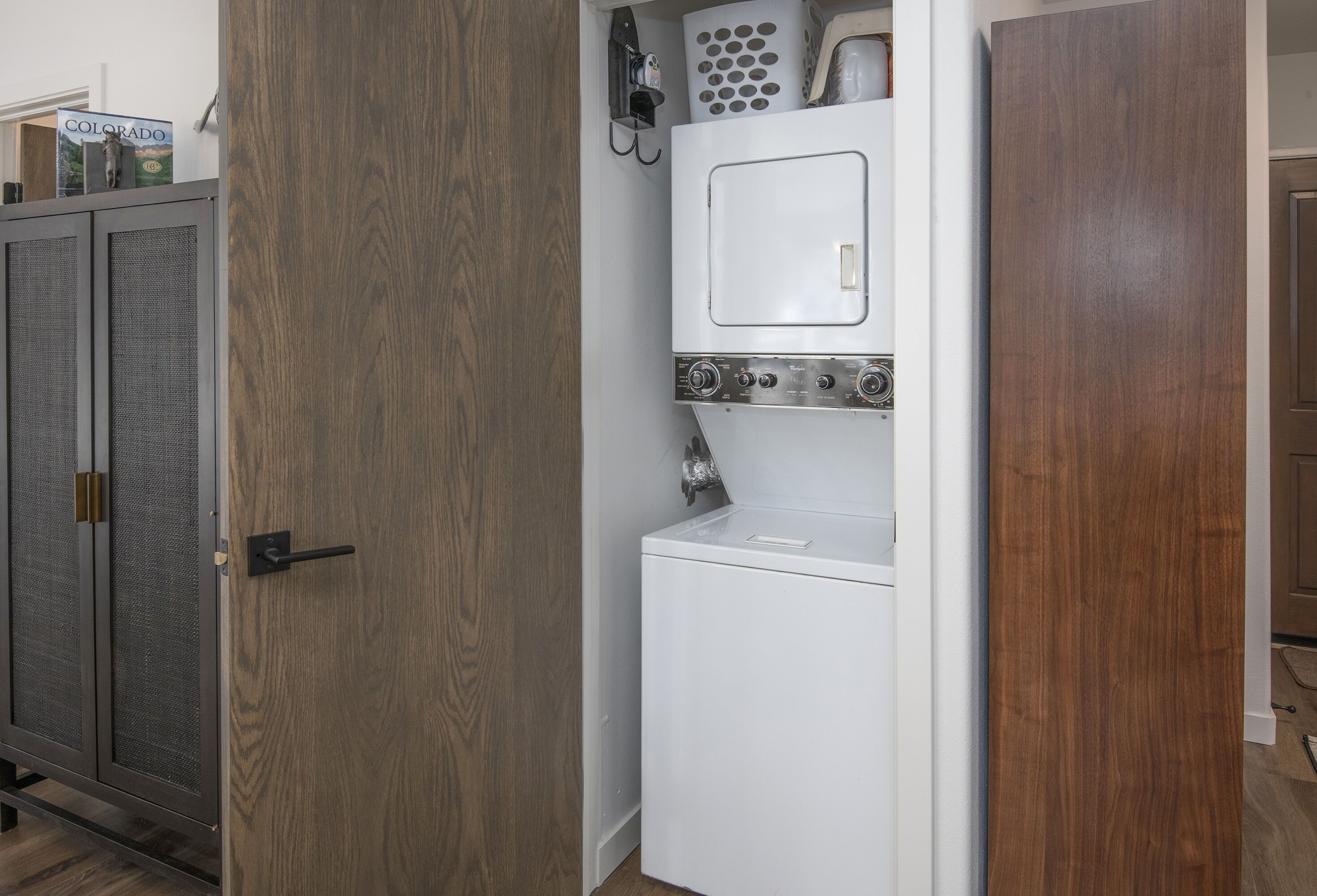 A laundry room with a white washing machine and dryer, a wooden door, and a metal cabinet.
