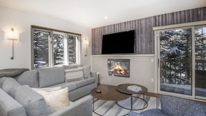 A modern living room with a fireplace, grey sofas, a coffee table, and large windows with a snowy view. - Beaver Creek Resort CO - Townsend Place Vacation Rentals (Avon)
