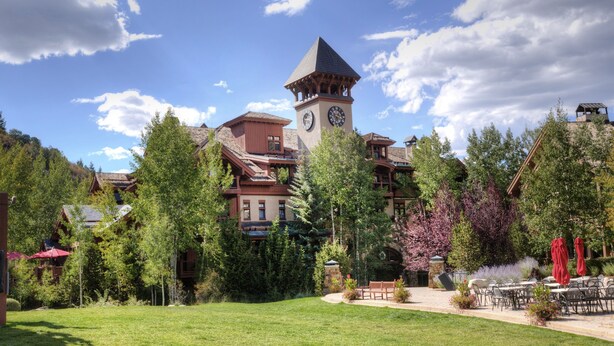 A lodge with a prominent clock tower, surrounded by lush greenery and a well-maintained lawn. - Edwards CO - Aspen Snowmasswood Lodge Vacation Rentals (Edwards)