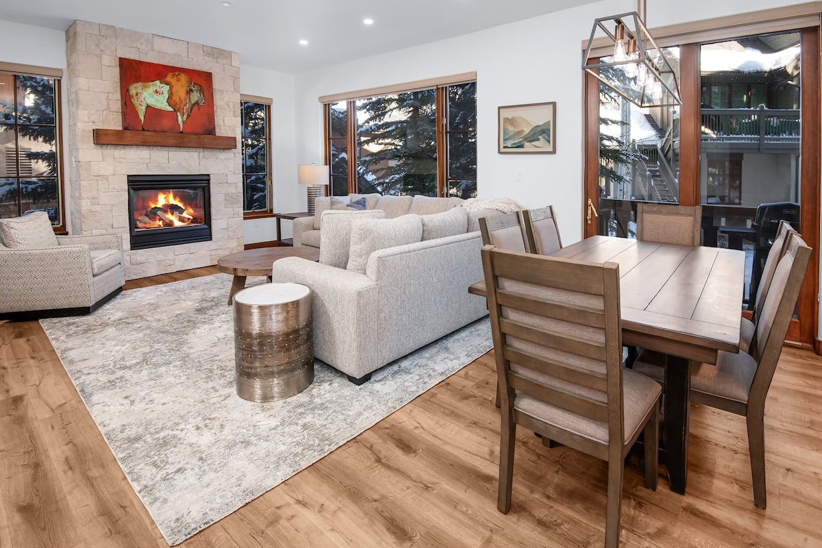 A modern living room with a fireplace, large windows, and a dining area.