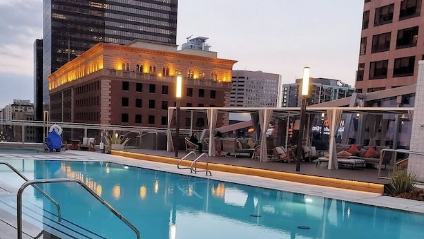 A rooftop pool with a clear view of the city skyline, including a prominent building with illuminated windows.