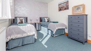 Una camera da letto con due letti, una cassettiera, una finestra con tende e una lampada a parete, oltre a un quadro incorniciato.