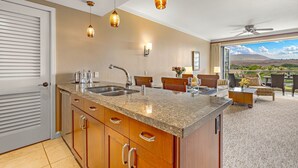 Una cocina con encimeras de granito, armarios de madera e iluminación colgante. Hay un comedor con mesa y sillas, y vistas al exterior.