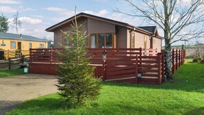 Een houten hut met een omheind erf, een kleine boom en een heldere lucht.