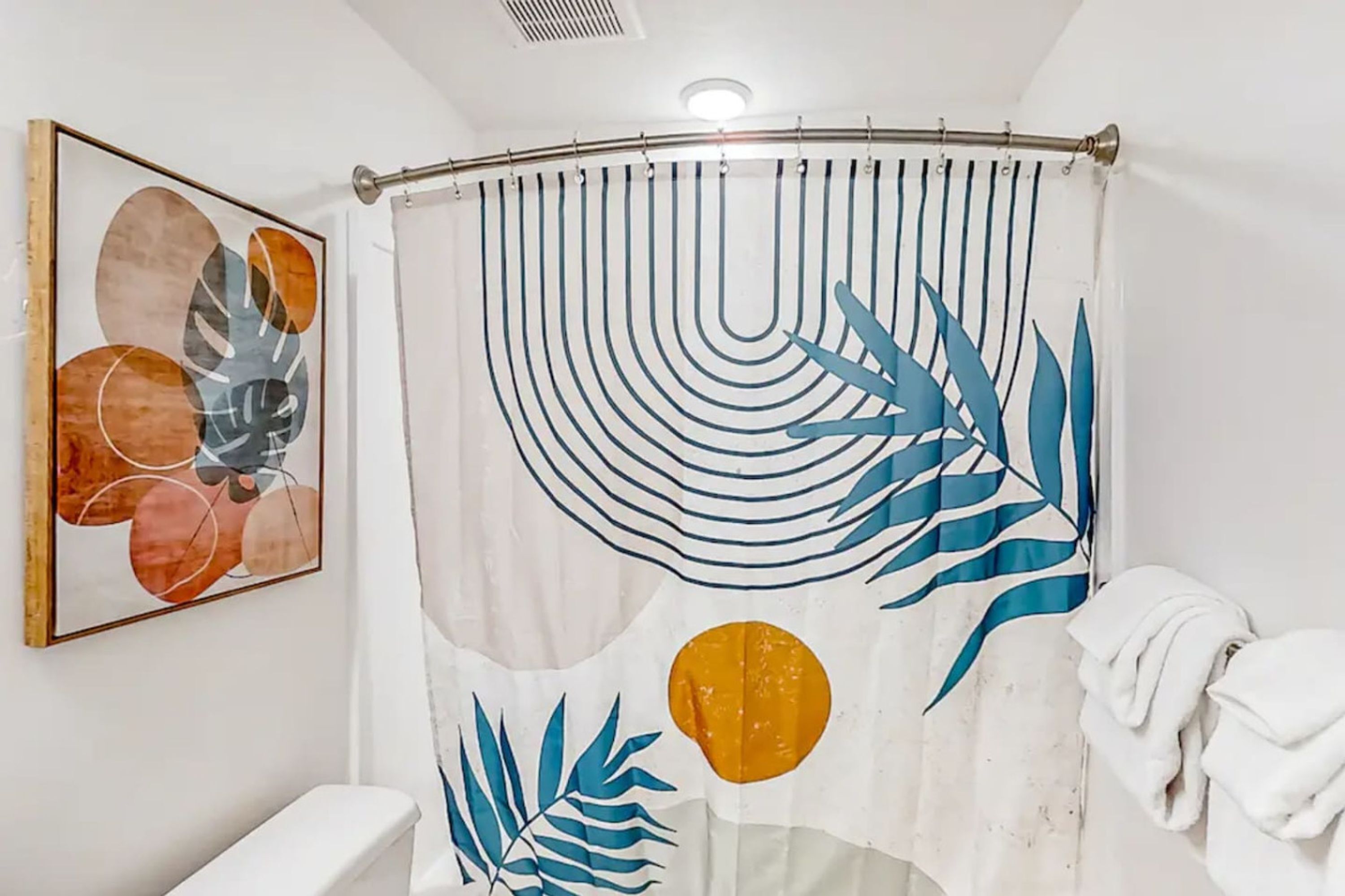 A bathroom with a shower curtain featuring leaf patterns, a toilet, and a framed abstract painting on the wall.