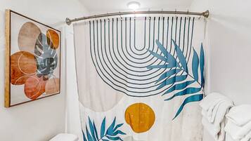 A bathroom with a shower curtain featuring leaf patterns, a toilet, and a framed abstract painting on the wall.