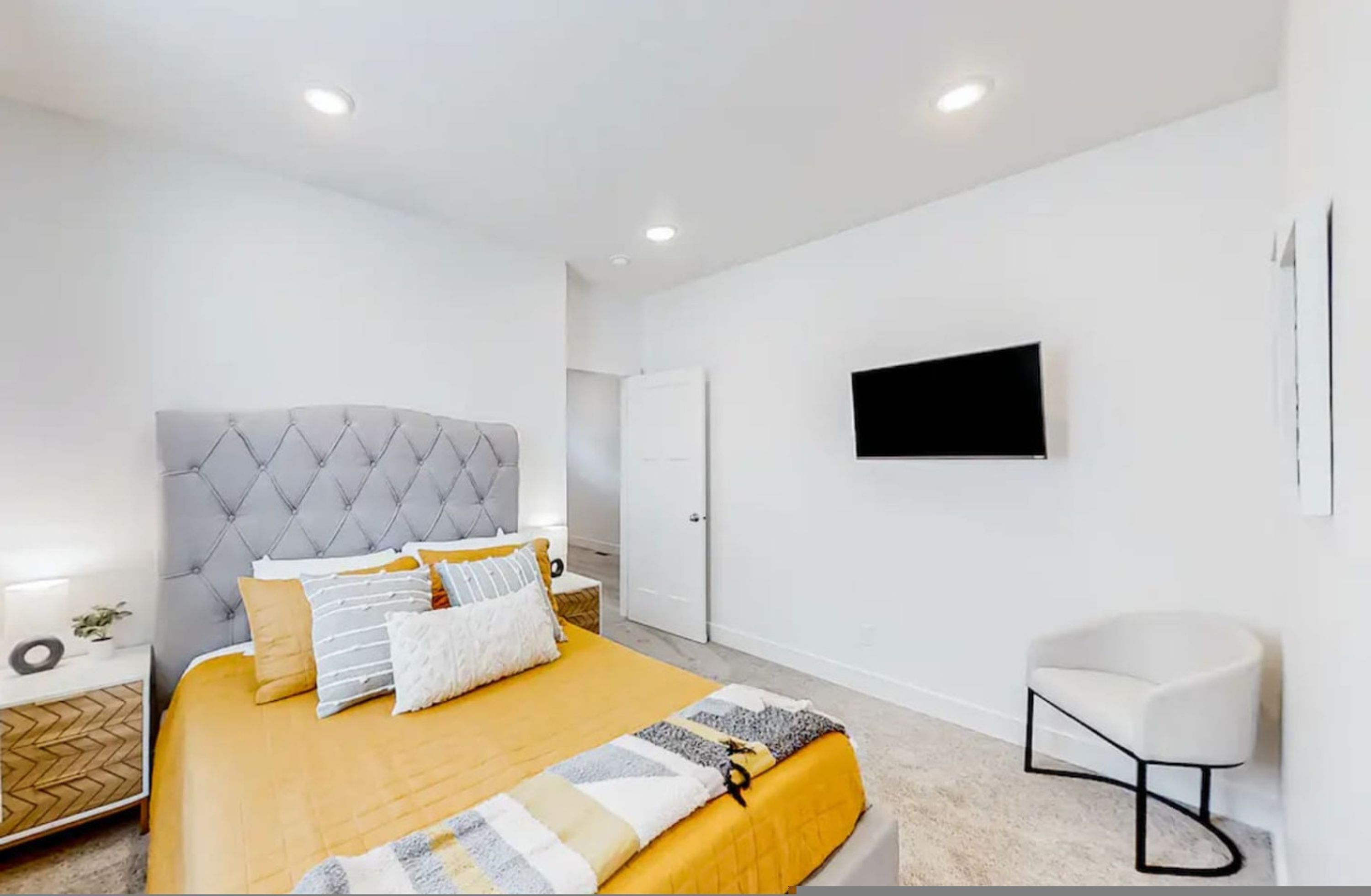 A modern bedroom with a bed, a TV mounted on the wall, and a white chair.