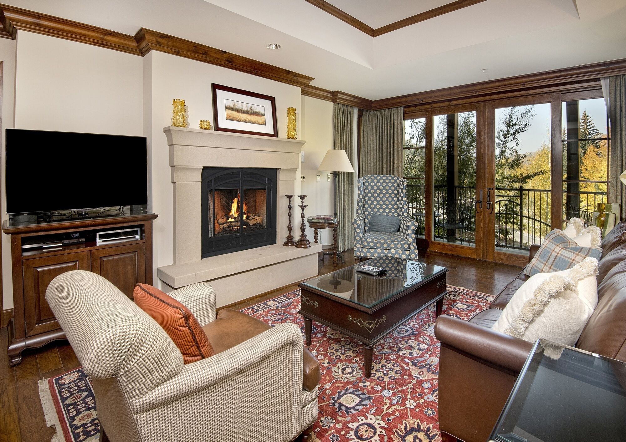 A living room with a fireplace, a television, and a large window with a view of trees.