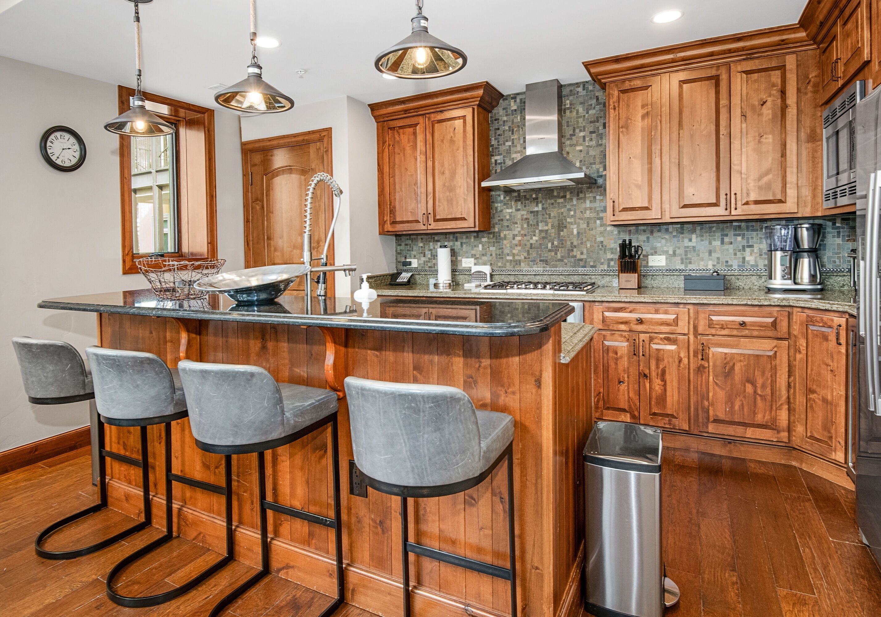 A kitchen with wooden cabinets, a bar area with stools, stainless steel appliances, and a tiled backsplash.