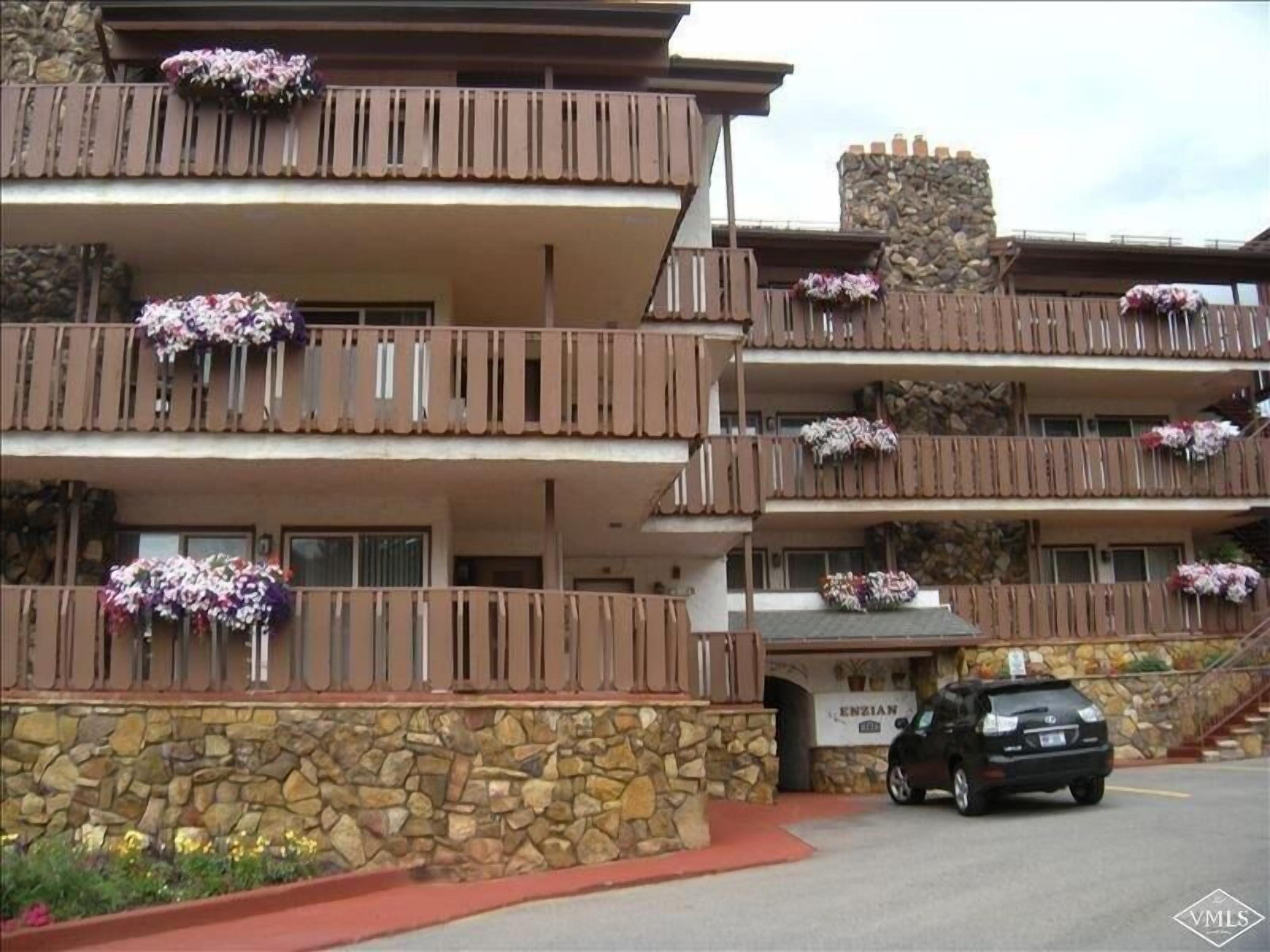 A multi-story hotel with balconies adorned with flowers, a stone facade, and a sign indicating the name 'ENZIAN'.
