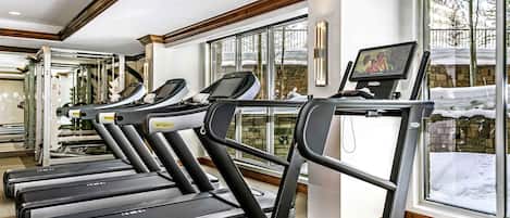 Varias cintas de correr en un gimnasio con grandes ventanales y vistas de nieve.