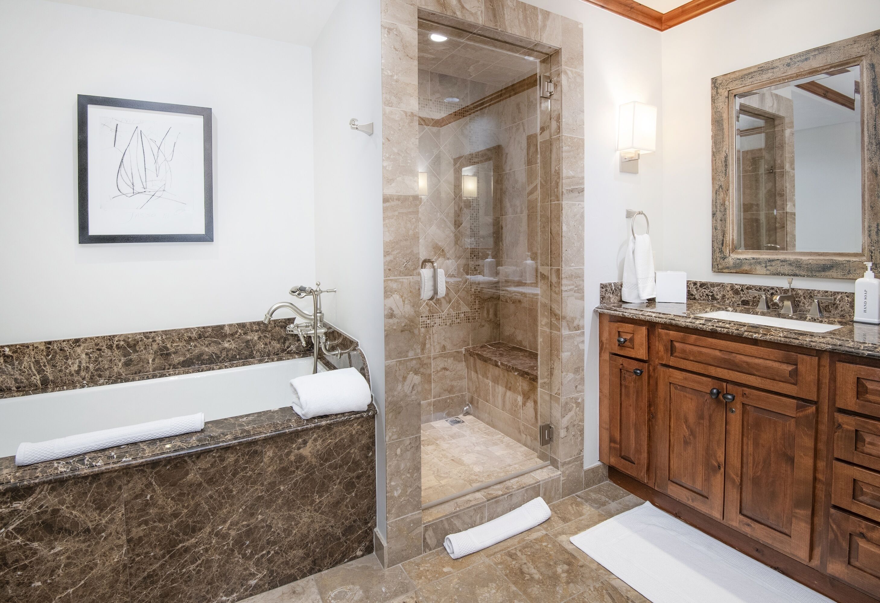 A bathroom with a marble sink, wooden cabinets, a large mirror, and a framed artwork on the wall.