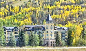 Un hotel a più piani con una torre centrale, immerso in un pendio boscoso.