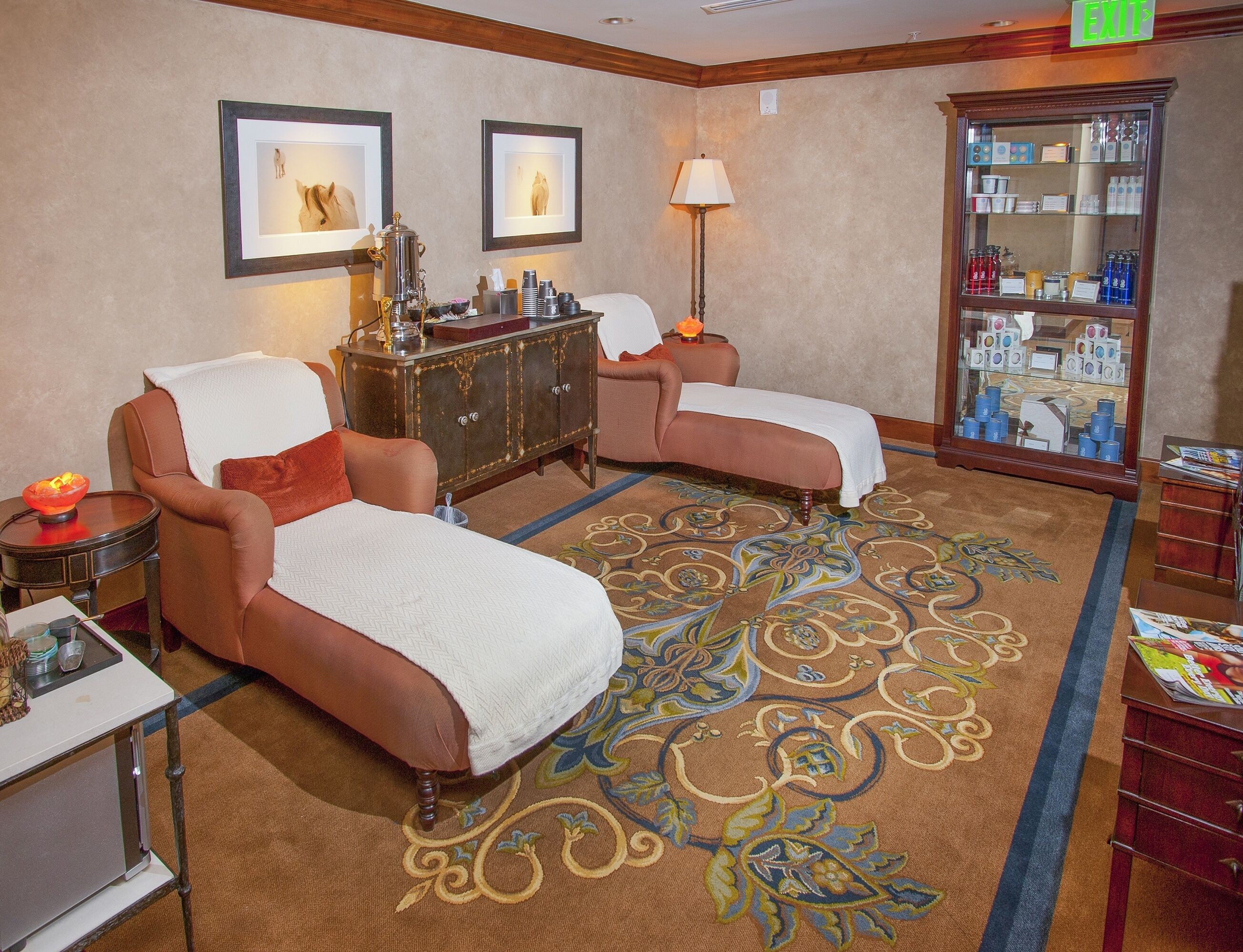 A hotel room with two sofas, a minibar, a patterned carpet, and framed artwork on the wall.