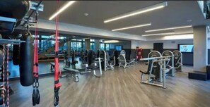 Ett modernt gym med olika typer av träningsutrustning, ett trägolv och stora fönster som släpper in naturligt ljus.