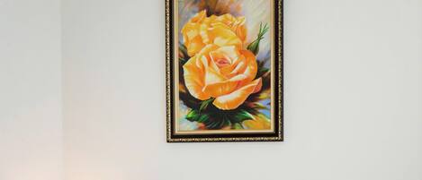 A hotel room with a red headboard, a painting of yellow roses, a pillow with the hotel's logo, and a bed with white linens and red towels.