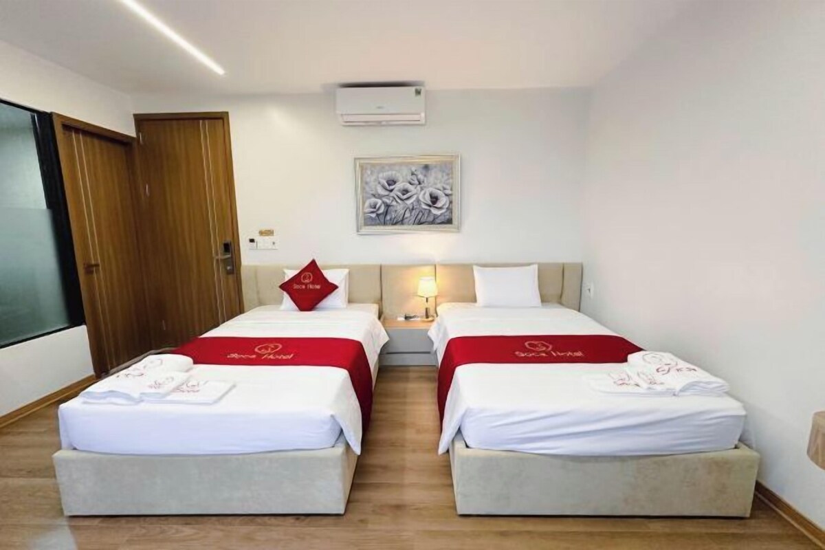 A hotel room with two beds, a wooden door, a wall-mounted air conditioner, and a framed artwork.